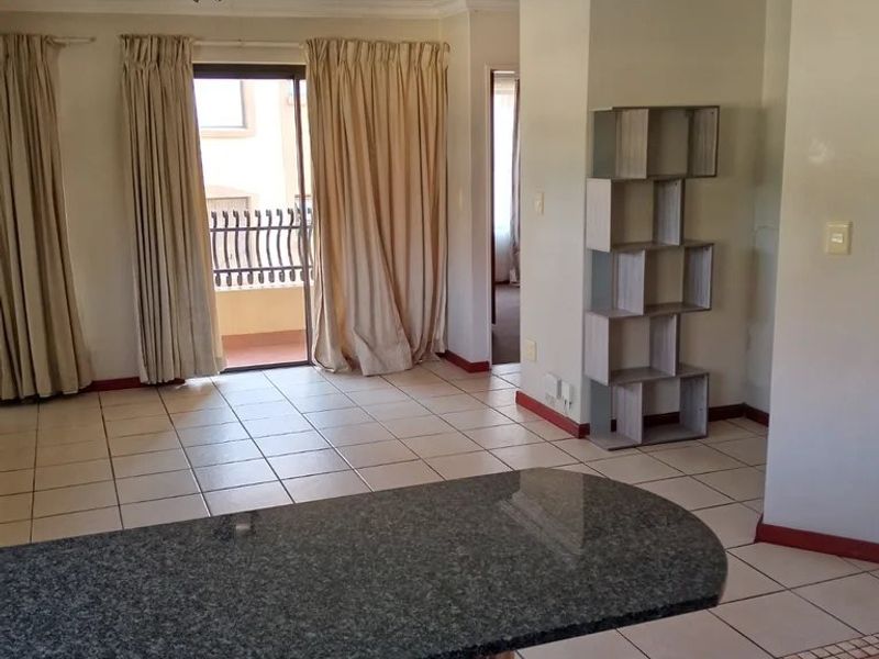 Open plan living area featuring ceramic tiled flooring, a granite breakfast bar, and direct access to a private balcony through sliding glass doors.