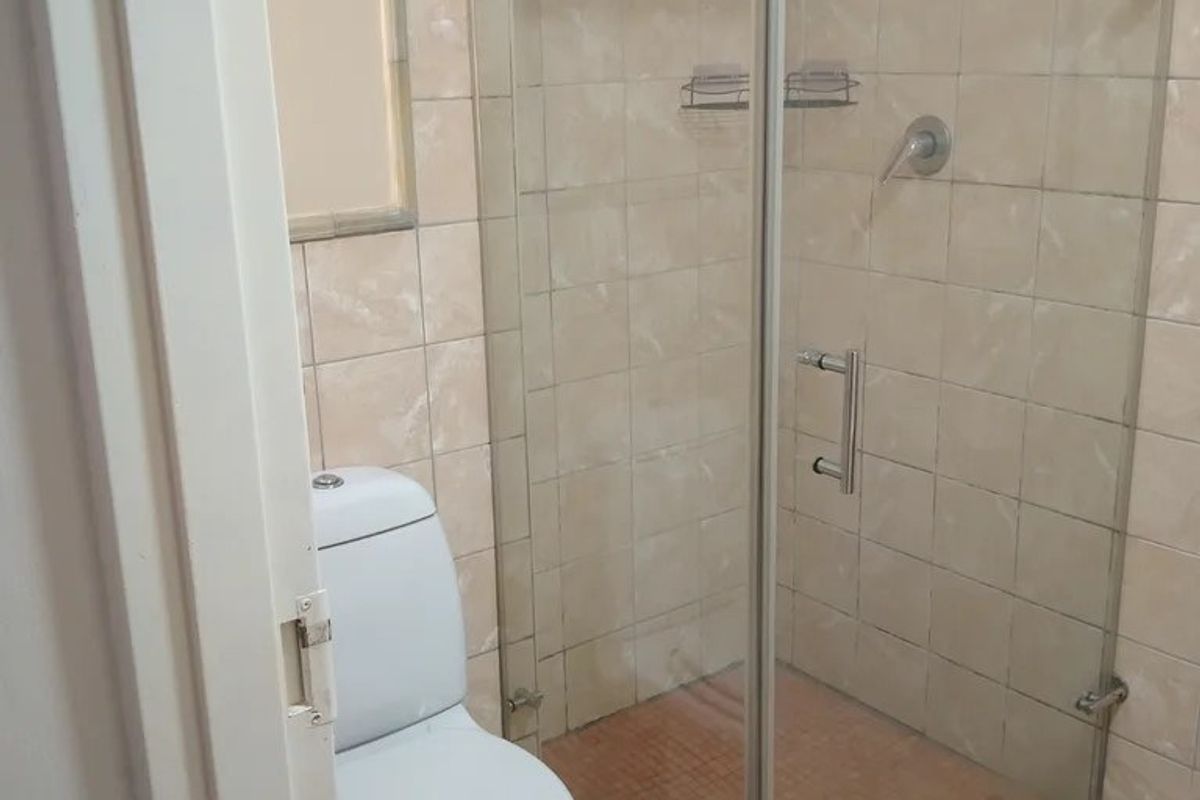 A functional bathroom featuring a glass-enclosed shower, ceramic tiling throughout, and a standard toilet suite.