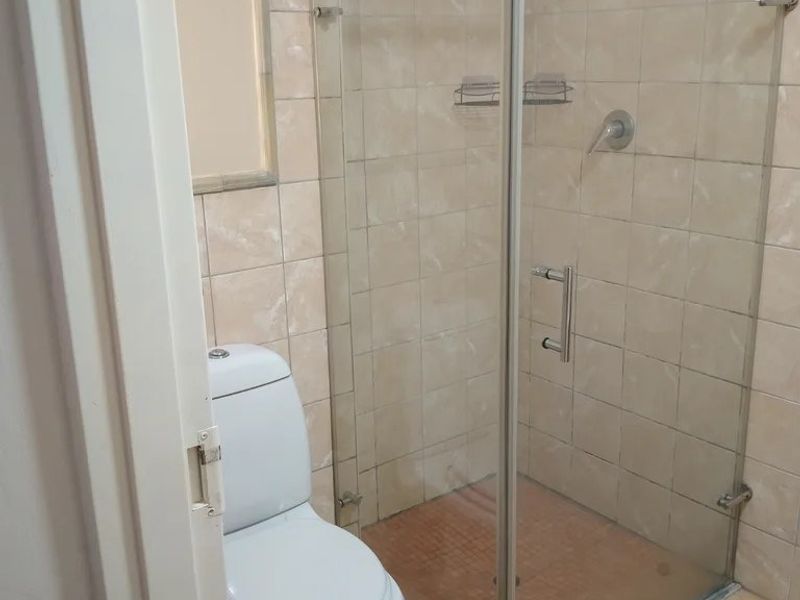 A functional bathroom featuring a glass-enclosed shower, ceramic tiling throughout, and a standard toilet suite.