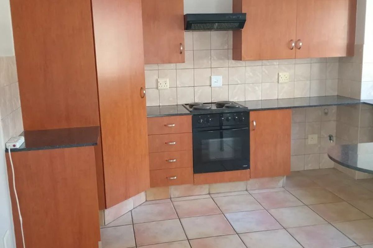 A functional kitchen featuring wood-look cabinetry, built-in oven and hob, tiled backsplash, and tiled flooring in a neutral, well-maintained space.