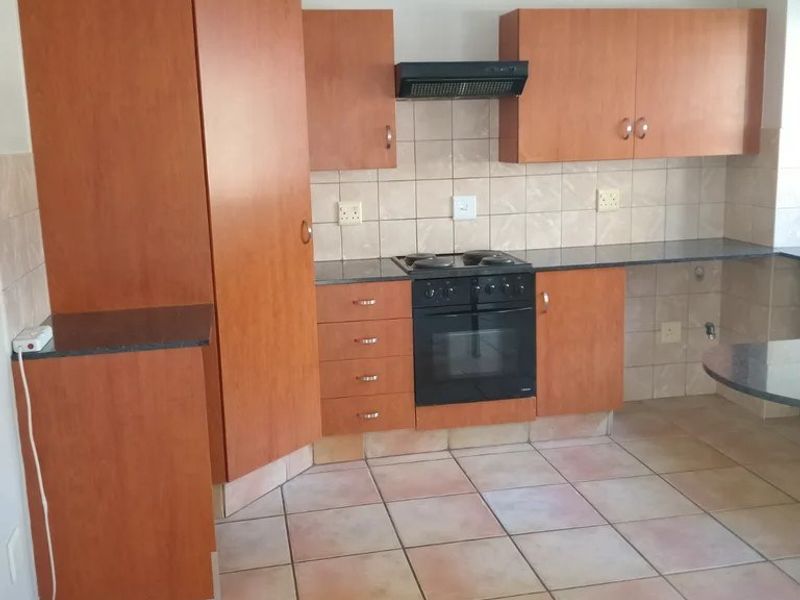 A functional kitchen featuring wood-look cabinetry, built-in oven and hob, tiled backsplash, and tiled flooring in a neutral, well-maintained space.