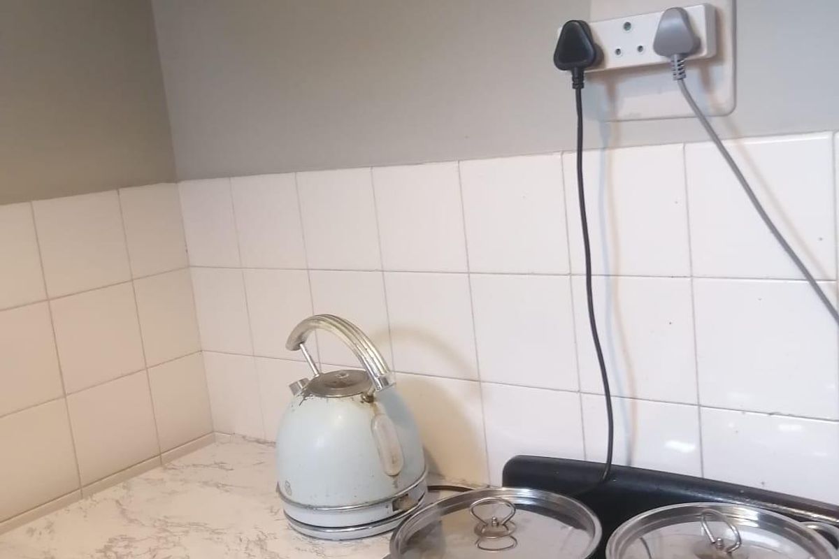 A compact kitchen area featuring a tiled splashback, laminate countertop, and wall-mounted cabinetry, showing signs of wear and dated finishes.