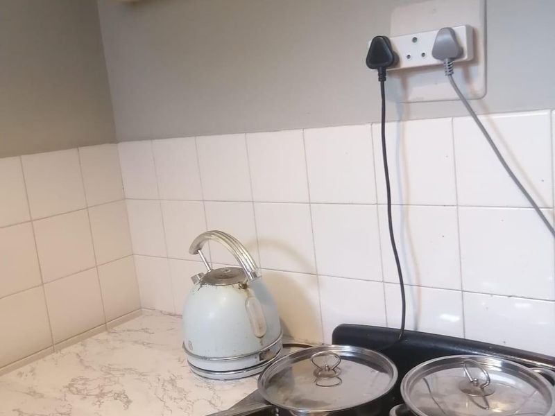A compact kitchen area featuring a tiled splashback, laminate countertop, and wall-mounted cabinetry, showing signs of wear and dated finishes.
