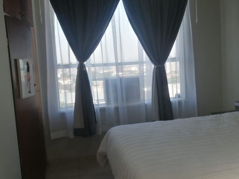 A bedroom featuring tiled flooring, a built-in wardrobe, and a window-mounted air conditioning unit.