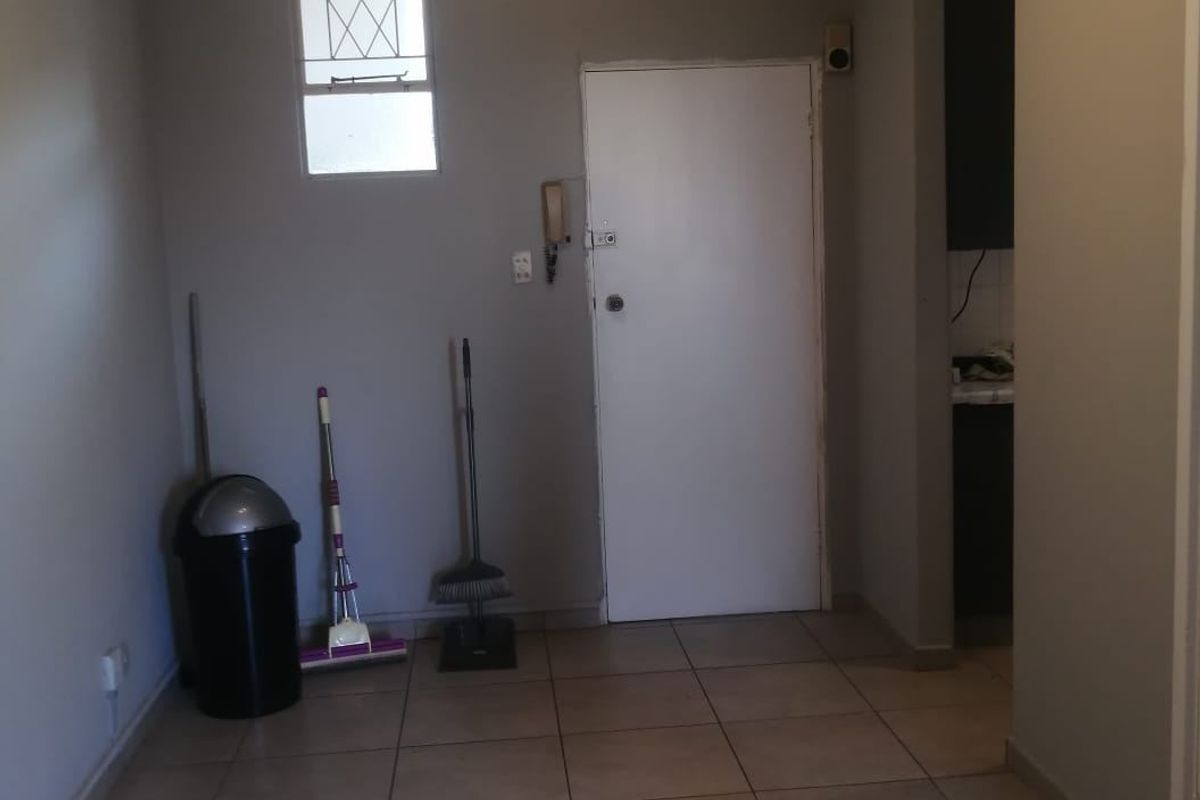 A functional entry area featuring tiled flooring, an intercom system, and a window with security bars, providing a clean canvas for potential interior updates.