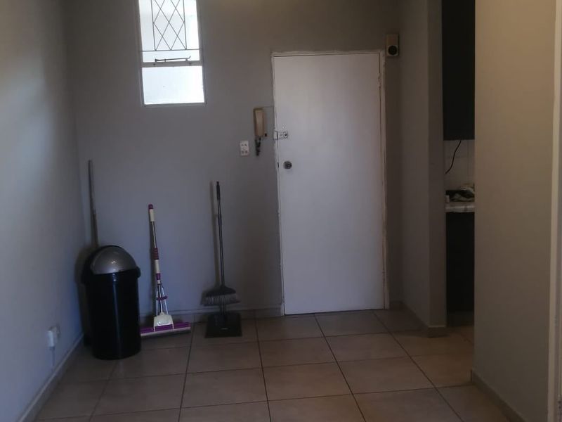 A functional entry area featuring tiled flooring, an intercom system, and a window with security bars, providing a clean canvas for potential interior updates.