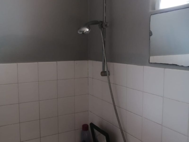 A functional bathroom featuring a bathtub with a handheld shower attachment, tiled splashback, and a basin.