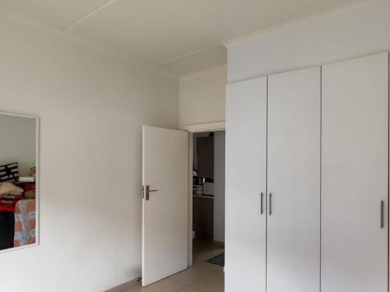 A bedroom featuring white built-in wardrobes, tiled flooring, and a neutral interior finish, providing a clean and functional living space.