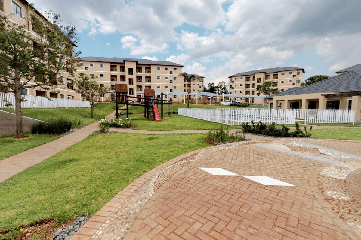 A well-maintained communal outdoor area featuring a swimming pool, paved walkways, landscaped gardens, and a playground within an apartment complex.