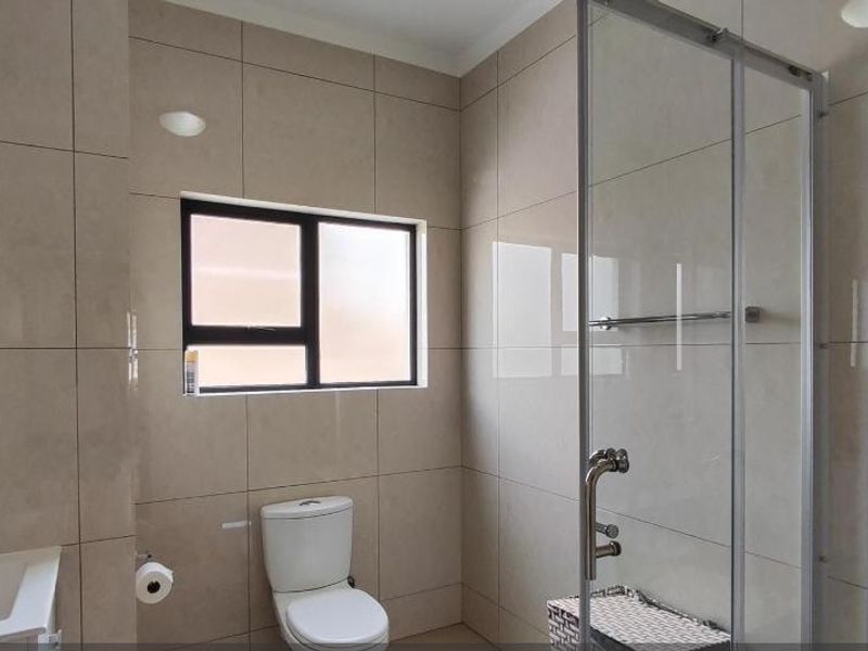 A modern, well-maintained bathroom featuring floor-to-ceiling neutral tiling, a glass shower enclosure, a wall-mounted vanity, and a toilet.
