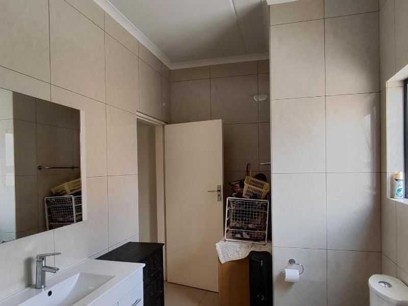 A functional bathroom featuring floor-to-ceiling wall tiles, a modern vanity with a basin, and a window providing natural light.