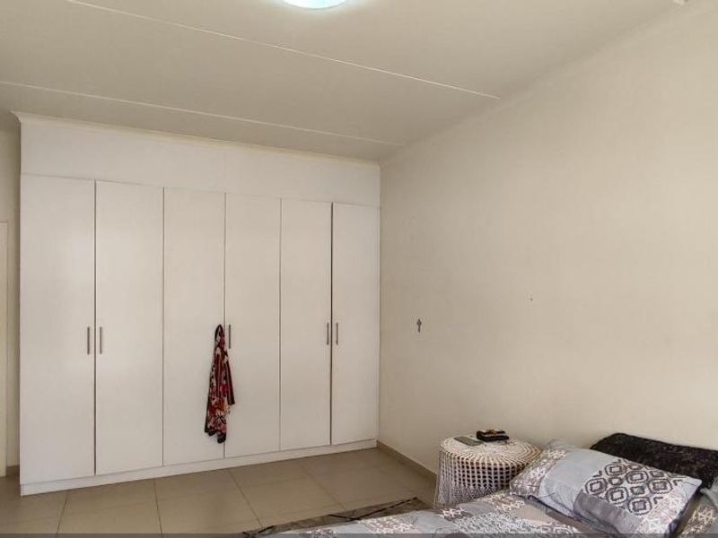 A bedroom featuring neutral tiled flooring and extensive white built-in cupboards providing ample storage space.