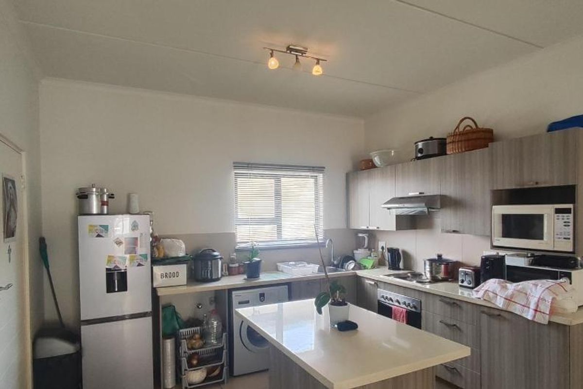 A functional kitchen featuring wood-look cabinetry, a central island, built-in oven with extractor fan, and tiled backsplash, offering practical storage and workspace.