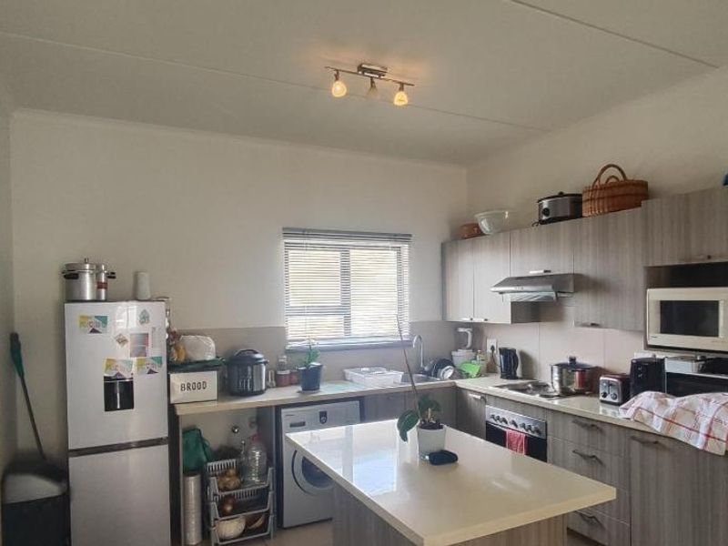 A functional kitchen featuring wood-look cabinetry, a central island, built-in oven with extractor fan, and tiled backsplash, offering practical storage and workspace.