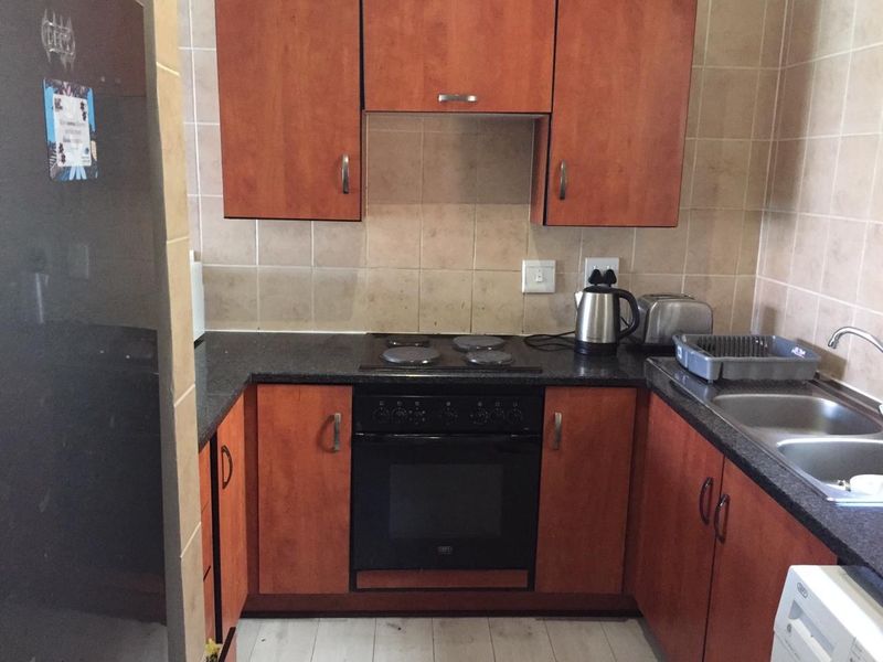 A compact kitchen featuring wooden cabinetry, dark laminate countertops, a built-in oven with electric hob, and a double bowl sink with tiled backsplash.