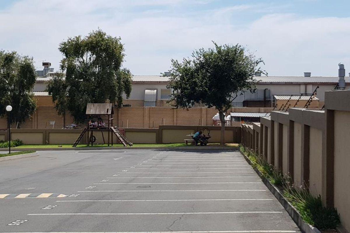 An exterior view of an apartment complex parking area featuring a perimeter boundary wall with integrated electric fencing and paved parking bays.