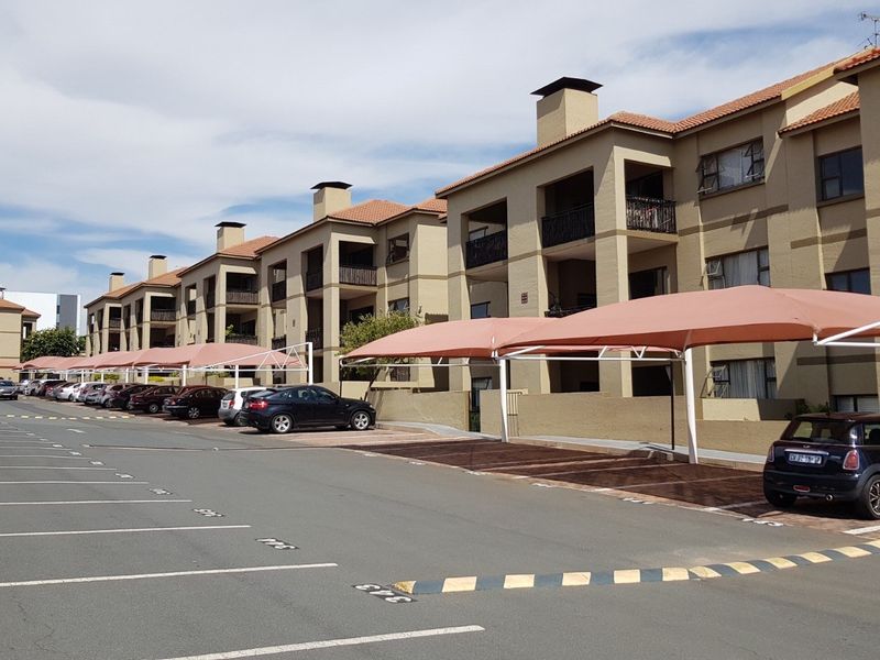 Exterior view of a multi-story apartment complex featuring covered parking bays and private balconies.