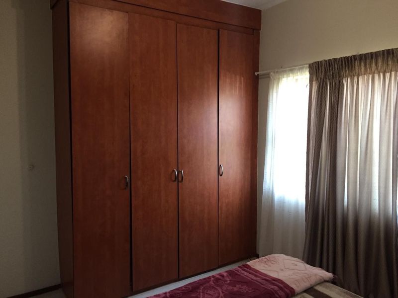 A bedroom featuring a large, full-height built-in wooden wardrobe and a window with curtains.