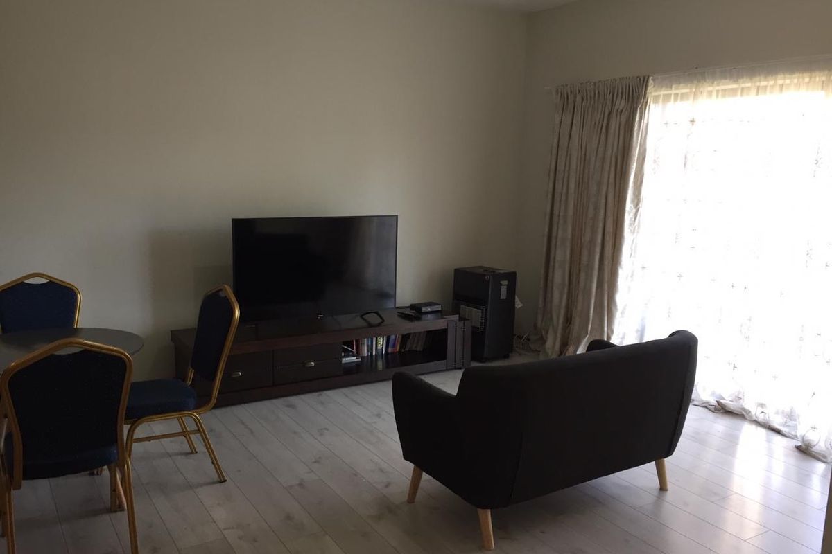 A living room area featuring light-toned laminate flooring and large windows with floor-to-ceiling curtains, providing natural light to the space.