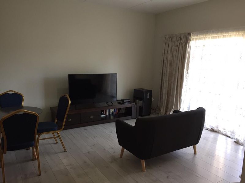 A living room area featuring light-toned laminate flooring and large windows with floor-to-ceiling curtains, providing natural light to the space.