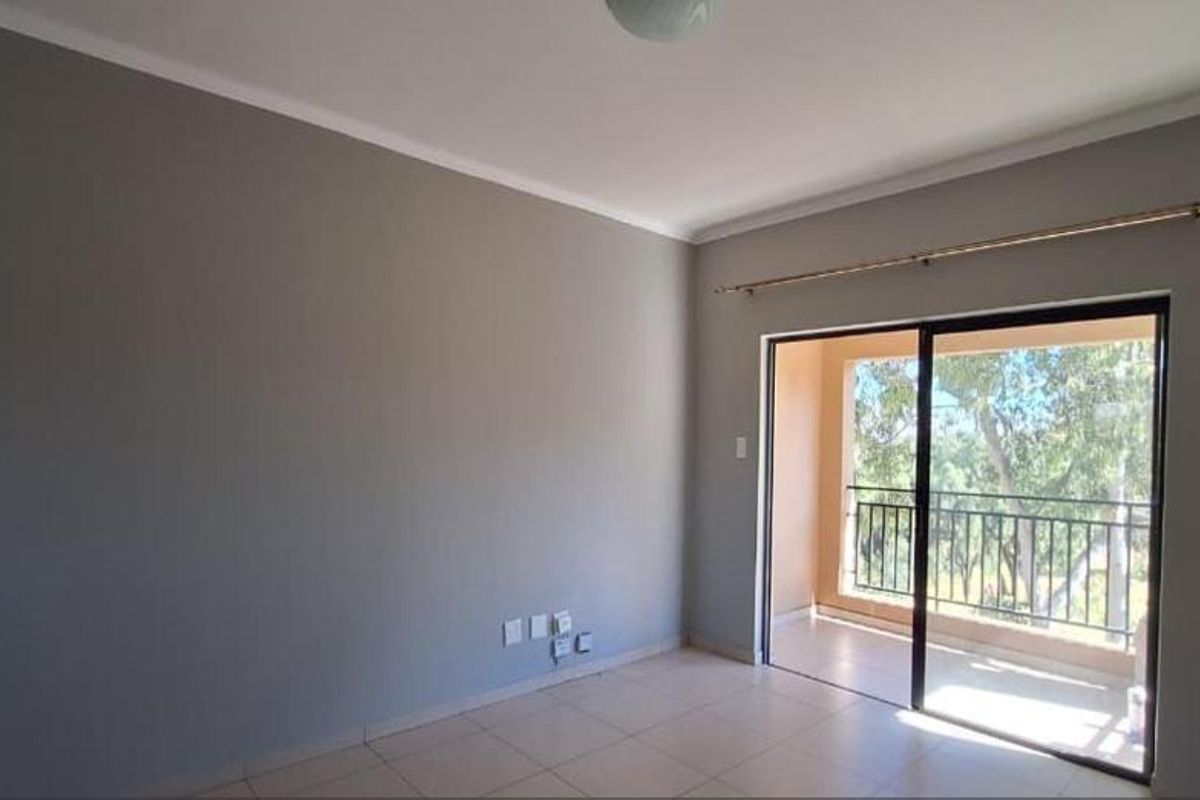 A bright, empty living room featuring neutral grey walls, tiled flooring, and a sliding glass door providing access to a private balcony.