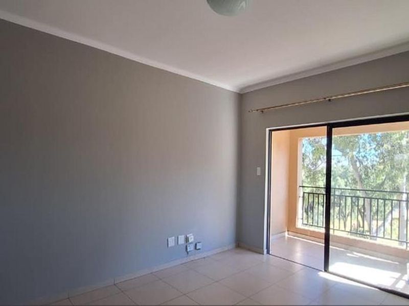A bright, empty living room featuring neutral grey walls, tiled flooring, and a sliding glass door providing access to a private balcony.