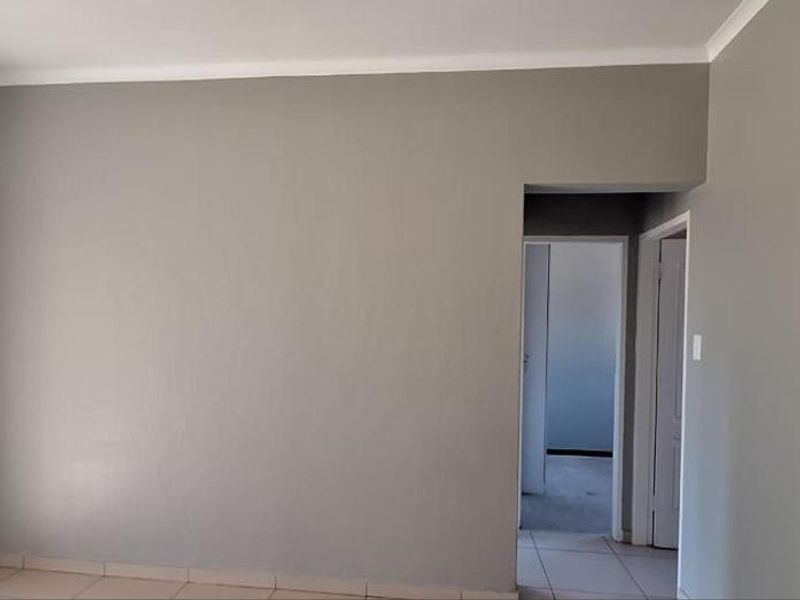 An empty open-plan living area featuring neutral grey walls, tiled flooring, and access to an outdoor balcony through a sliding glass door.