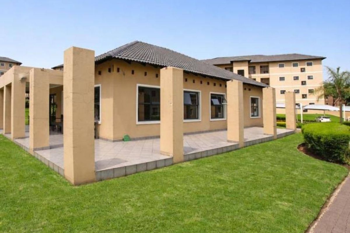 A well-maintained rear exterior view of the apartment featuring a spacious tiled patio with concrete pillars and a neatly landscaped lawn.