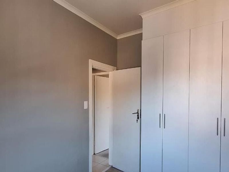 A clean, neutral bedroom featuring ample built-in cupboard storage and classic coving detail.