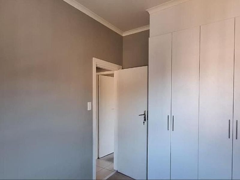 A clean, neutral bedroom featuring ample built-in cupboard storage and classic cornice detailing, offering a blank canvas for personalization.
