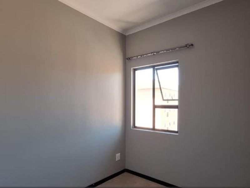 A clean, empty bedroom featuring neutral grey walls, a casement window with a curtain rod, and built-in cupboard storage.