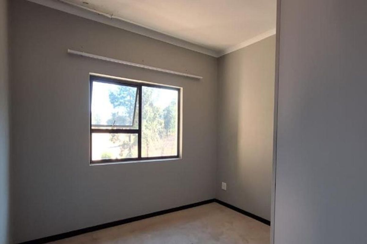 A clean, empty bedroom featuring neutral grey walls, a large aluminium window, and simple coving, providing a blank canvas for personalization.