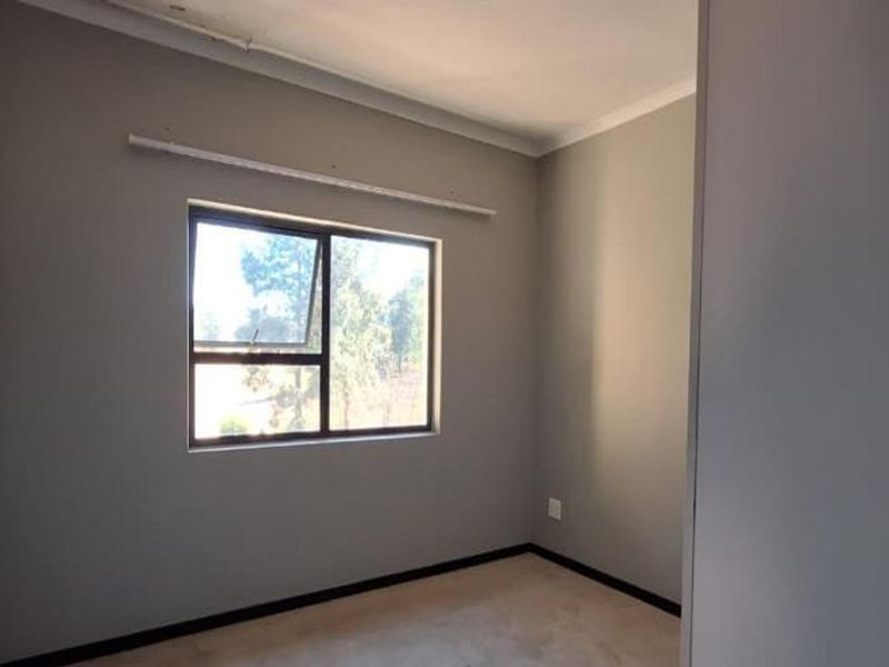 A clean, empty bedroom featuring neutral grey walls, a large aluminium window, and simple coving, providing a blank canvas for personalization.