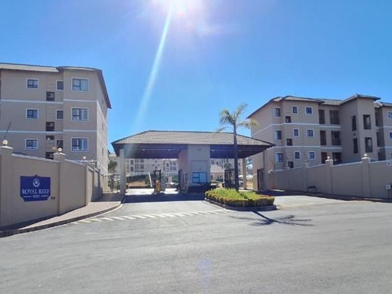 The entrance to Royal Reef apartment complex featuring a secure gatehouse, perimeter walling, and multi-story residential buildings.