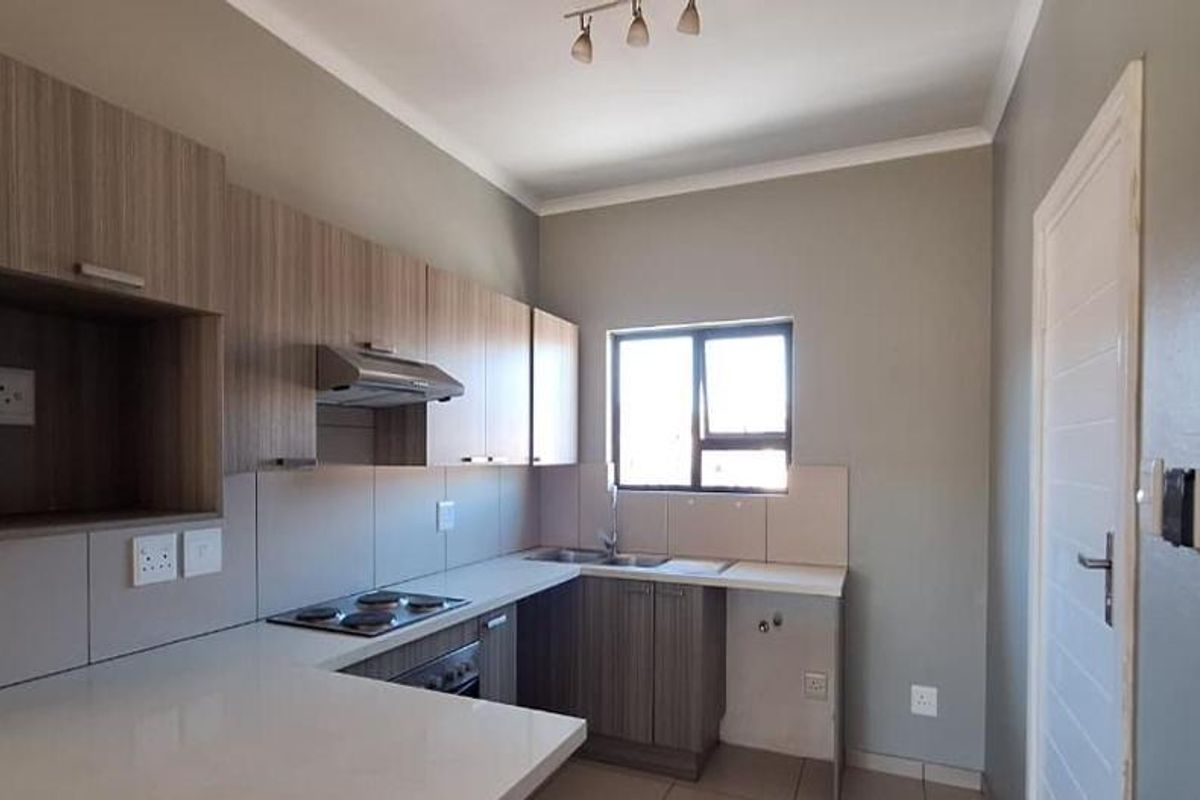 A modern, clean kitchen featuring light wood-tone cabinetry, stone countertops, an integrated electric hob, and a stainless steel sink with tiled splashbacks.
