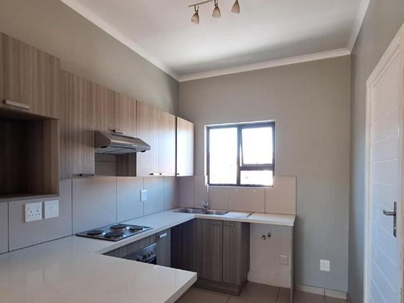 A modern, clean kitchen featuring light wood-tone cabinetry, stone countertops, an integrated electric hob, and a stainless steel sink with tiled splashbacks.