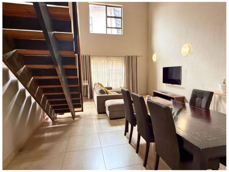Spacious open-plan living and dining area featuring a modern staircase, double-volume ceilings, and large windows providing ample natural light.