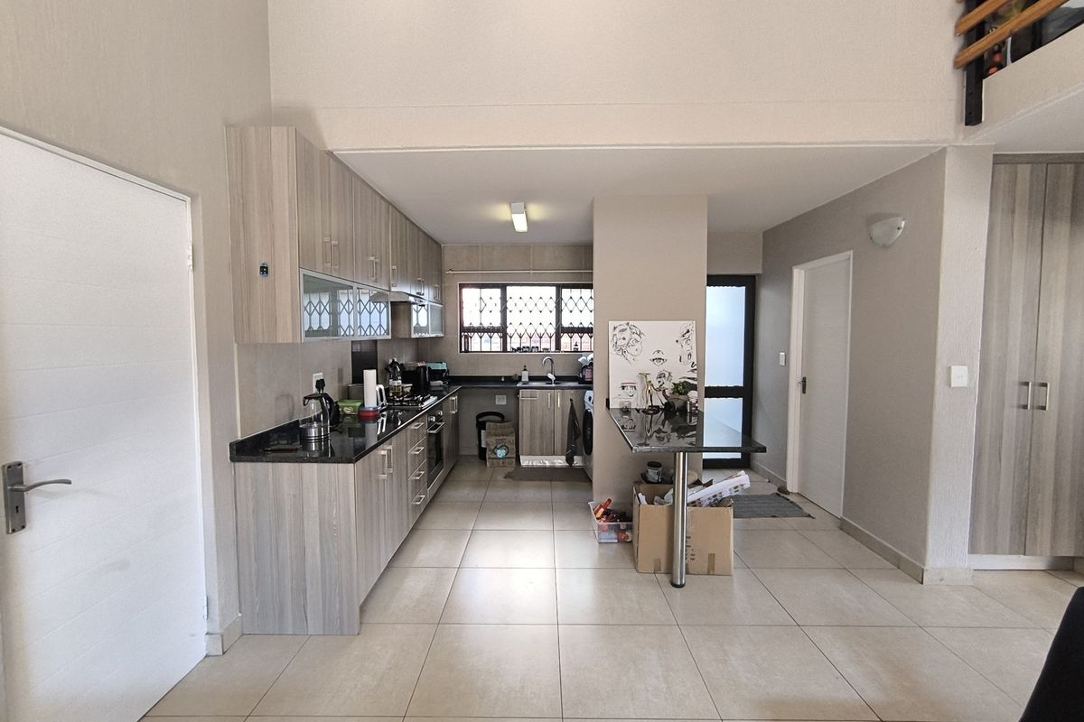 A functional kitchen featuring modern wood-look cabinetry, granite countertops, built-in appliances, and a breakfast bar, set within an open-plan living space.