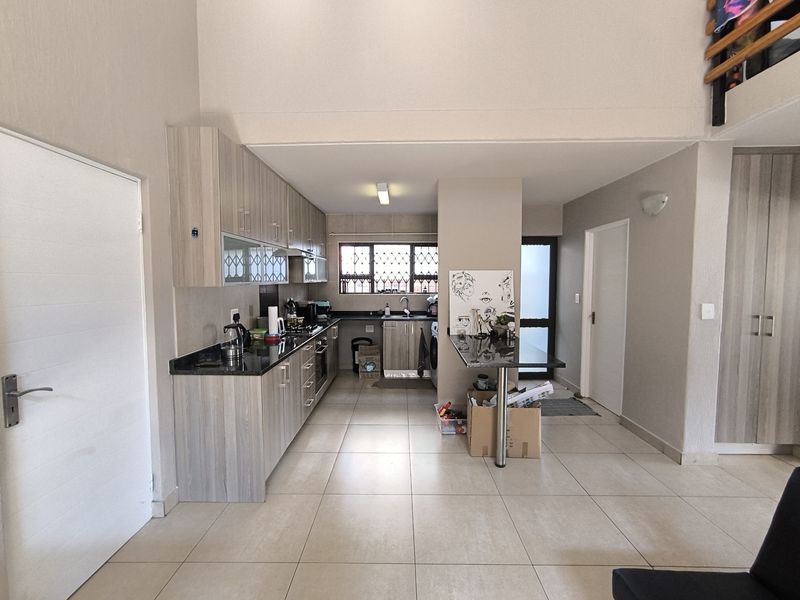 A functional kitchen featuring modern wood-look cabinetry, granite countertops, built-in appliances, and a breakfast bar, set within an open-plan living space.