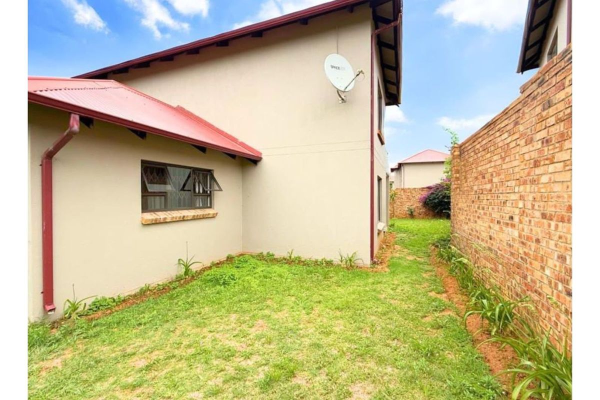 Rear exterior view of the townhouse featuring a private garden area, brick boundary wall, and corrugated metal roofing.