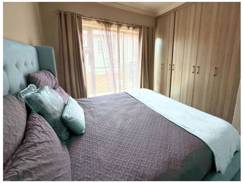 A bedroom featuring built-in wooden cupboards and a window providing natural light.