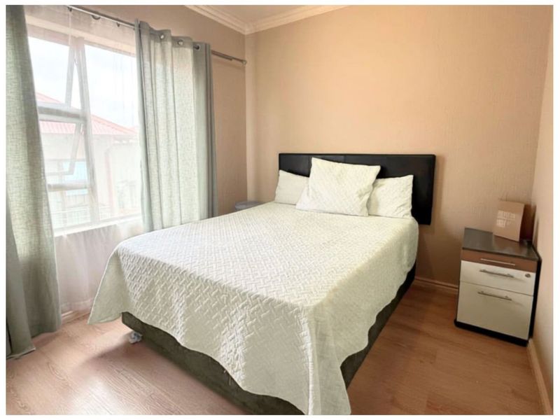 A standard bedroom featuring laminate flooring, neutral wall finishes, and an aluminium window frame.