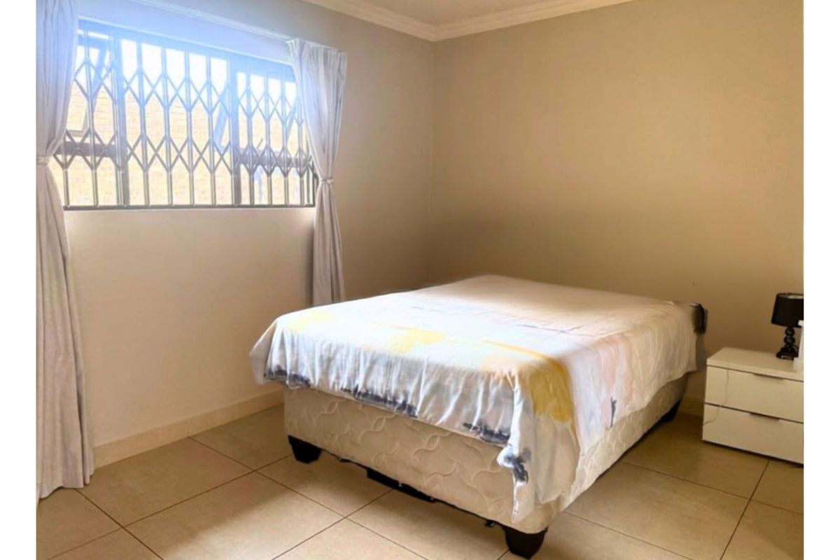 A bedroom featuring tiled flooring, neutral wall finishes, and a window fitted with a security gate.
