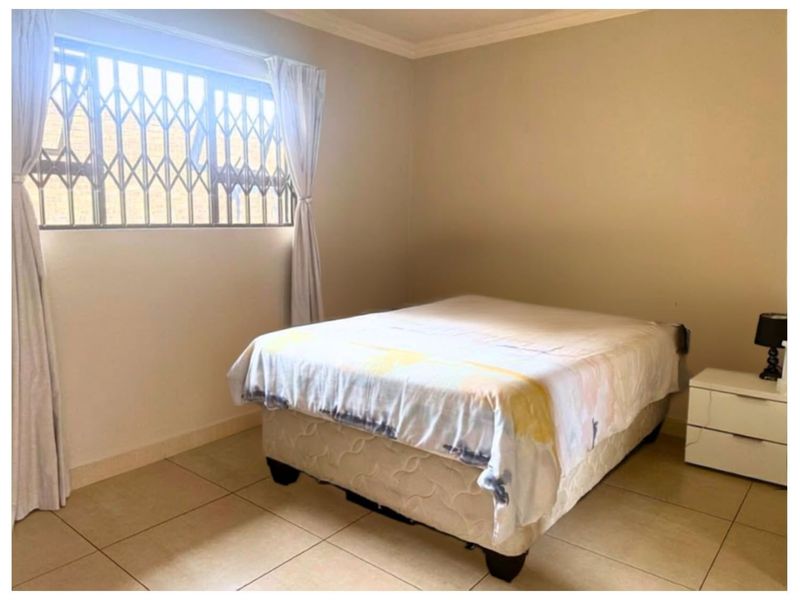 A bedroom featuring tiled flooring, neutral wall finishes, and a window fitted with a security gate.