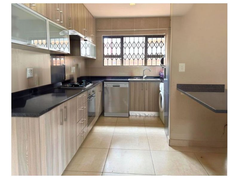 Functional kitchen featuring laminate cabinetry, granite countertops, built-in oven, gas hob, and a breakfast bar, with tiled flooring and a secure window.