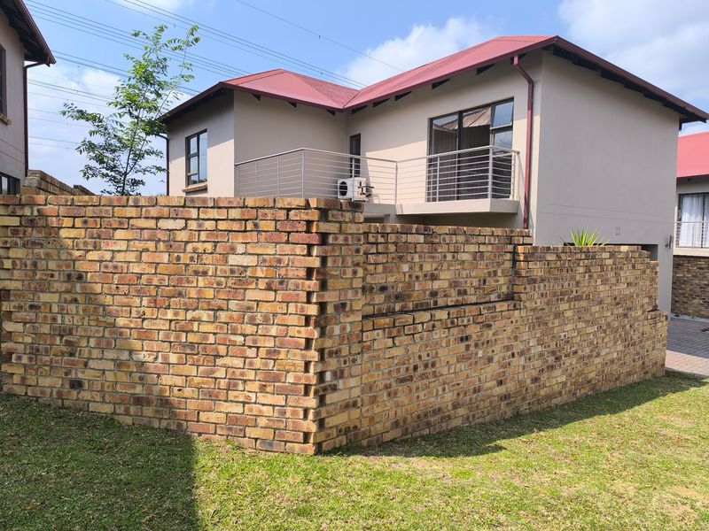 Rear view of a townhouse featuring a face brick boundary wall, a metal balcony railing, and a red metal roof.