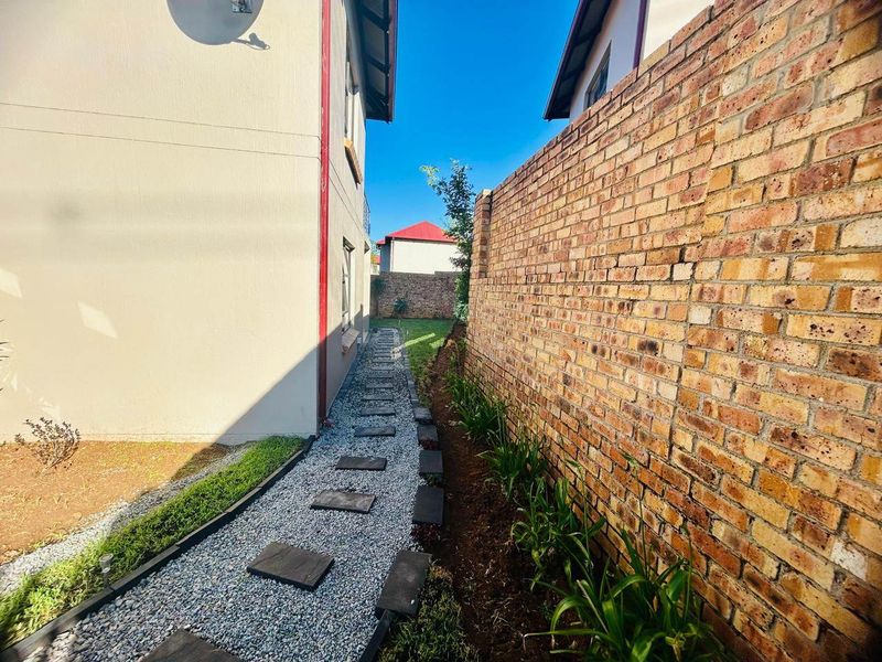 A side garden pathway featuring gravel, stone pavers, and a brick boundary wall along the side of the townhouse.