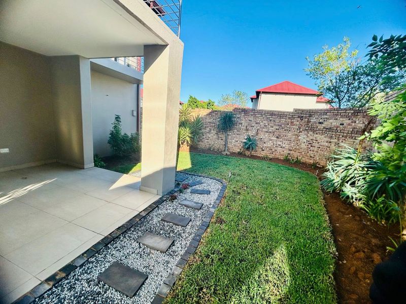 A well-maintained rear garden featuring a covered patio, tiled flooring, and a neat lawn with decorative stone pathways and brick boundary walls.