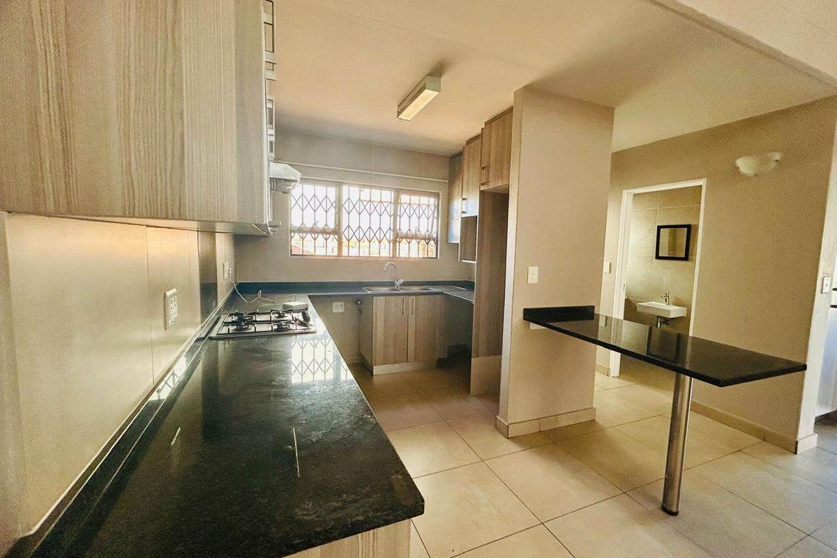 Modern kitchen featuring light wood cabinetry, dark granite countertops, a gas hob, and an integrated breakfast bar, leading to an adjacent bathroom area.