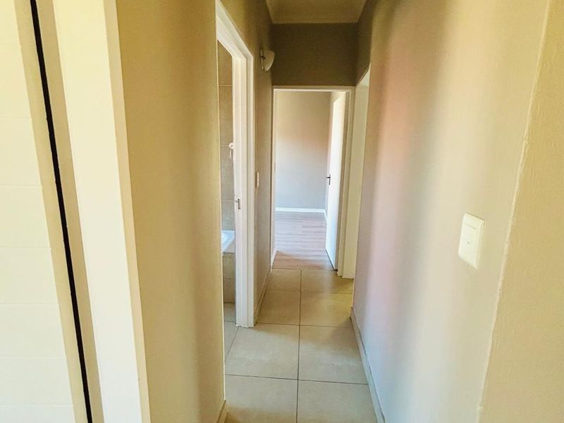 A clean, neutral-toned hallway featuring tiled flooring and providing access to adjacent rooms within the townhouse.